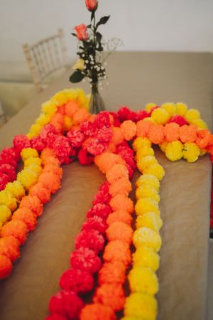 Vibrant paper flower garland in red, orange and yellow colors arranged on a table with roses in a vase.