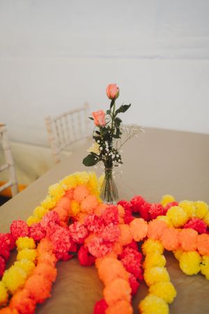 Colorful tissue paper pom pom garland with coral roses in clear vase centerpiece.