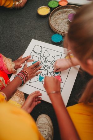 Overhead view of hands working together to color an intricate mandala pattern.