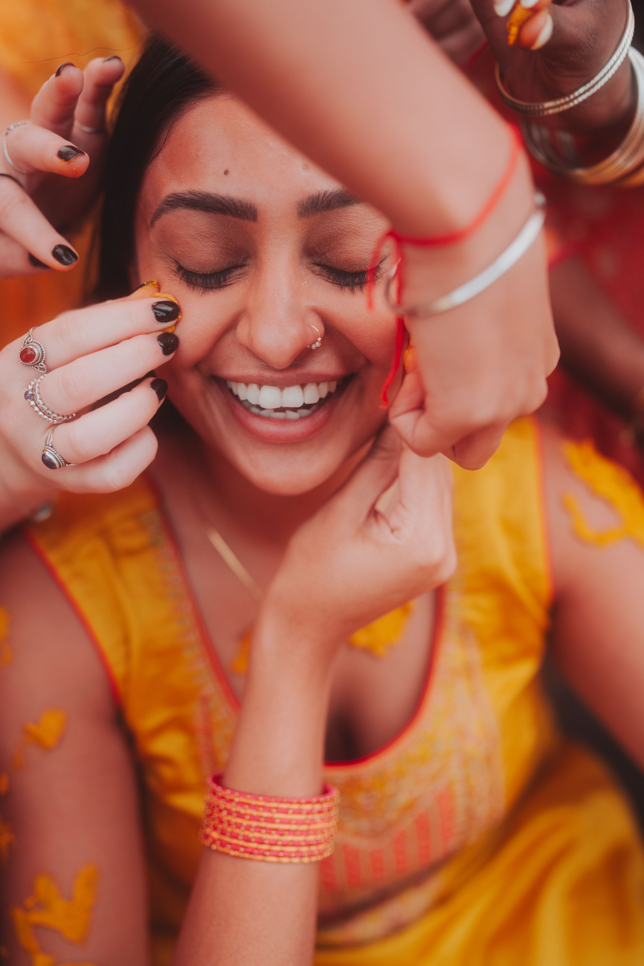 Close-up of someone wearing traditional Indian attire laughing while others apply decorative elements.