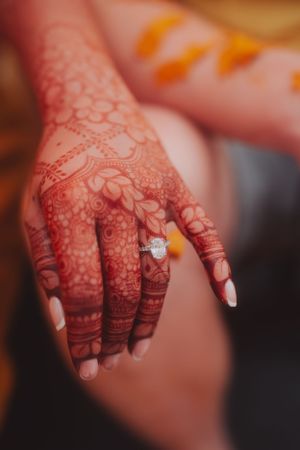 Detailed mehndi design on hand with diamond engagement ring.