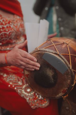 Someone plays a traditional drum while wearing ornate red traditional clothing.