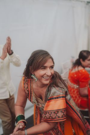 A person in vibrant orange and gold traditional attire dances at a celebration.