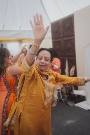 A person in yellow traditional attire dances with raised arms at a celebration.