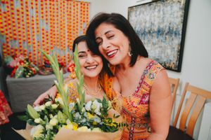 Two people smiling and posing with yellow flowers against an orange and white backdrop.