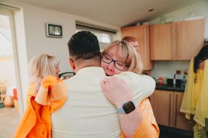 Emotional group hug shared in a bright kitchen setting.