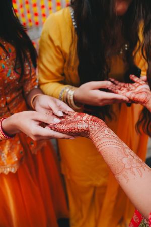Detailed henna mehndi art being applied on hands during traditional Indian ceremony.