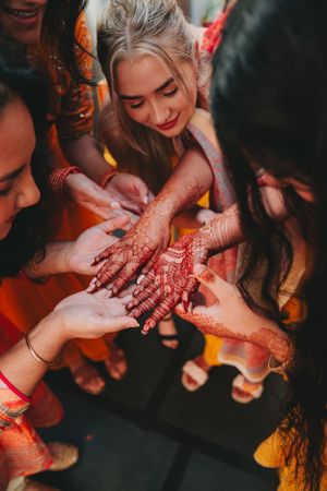 Hands gathering to admire intricate henna designs during celebration.