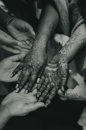 Black and white photo showing detailed mehndi designs on hands surrounded by supporters.