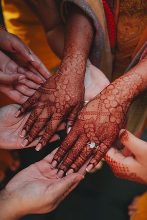 Intricate henna designs adorning hands with a diamond engagement ring during a traditional Indian wedding ceremony.