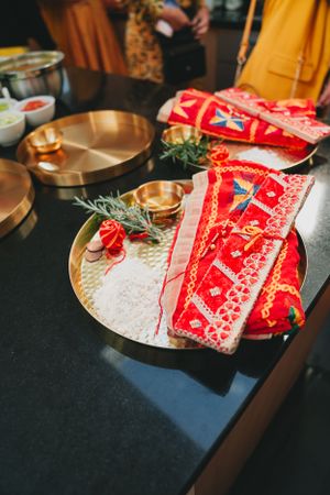 Traditional Indian wedding decorations with red fabric and brass plates arranged on a dark surface.