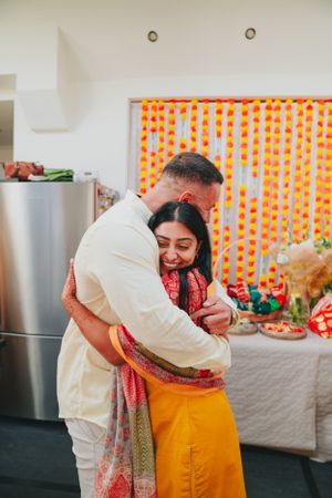 Couple embracing in front of orange marigold decorations during an Indian celebration.