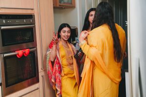 Women in vibrant yellow and red traditional Indian attire gathered in a kitchen.