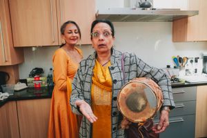 Two people sharing a lively moment with traditional drums in a kitchen setting.