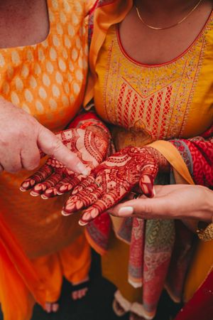 Close-up of intricate henna designs being applied to hands during a traditional Indian ceremony.