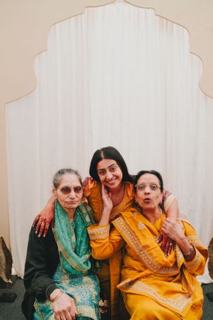 Three generations pose together against a white backdrop wearing traditional Indian clothing.