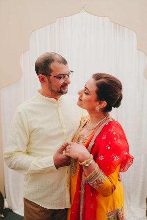 A couple shares an intimate moment while dressed in formal Indian attire against a white backdrop.