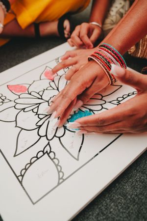 Hands adorned with bangles working on a detailed floral mandala coloring page.