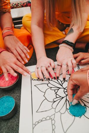 Multiple hands collaborating on coloring a large mandala design with vibrant powders.