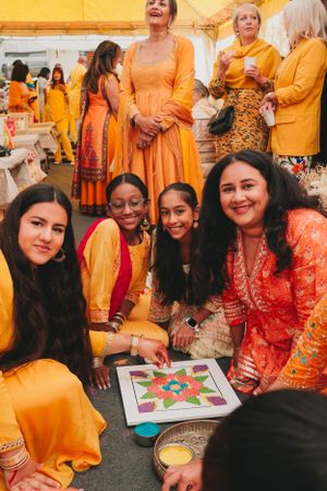 Participants in vibrant orange and red attire gathered around a colorful mandala art project.