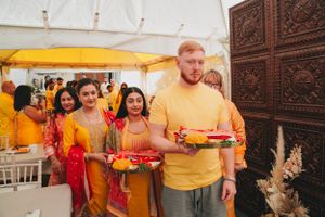 Line of attendees in orange and red attire carrying ceremonial plates at an indoor event.