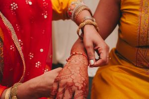 Close-up of intricate henna design being applied to hands during traditional Indian ceremony.