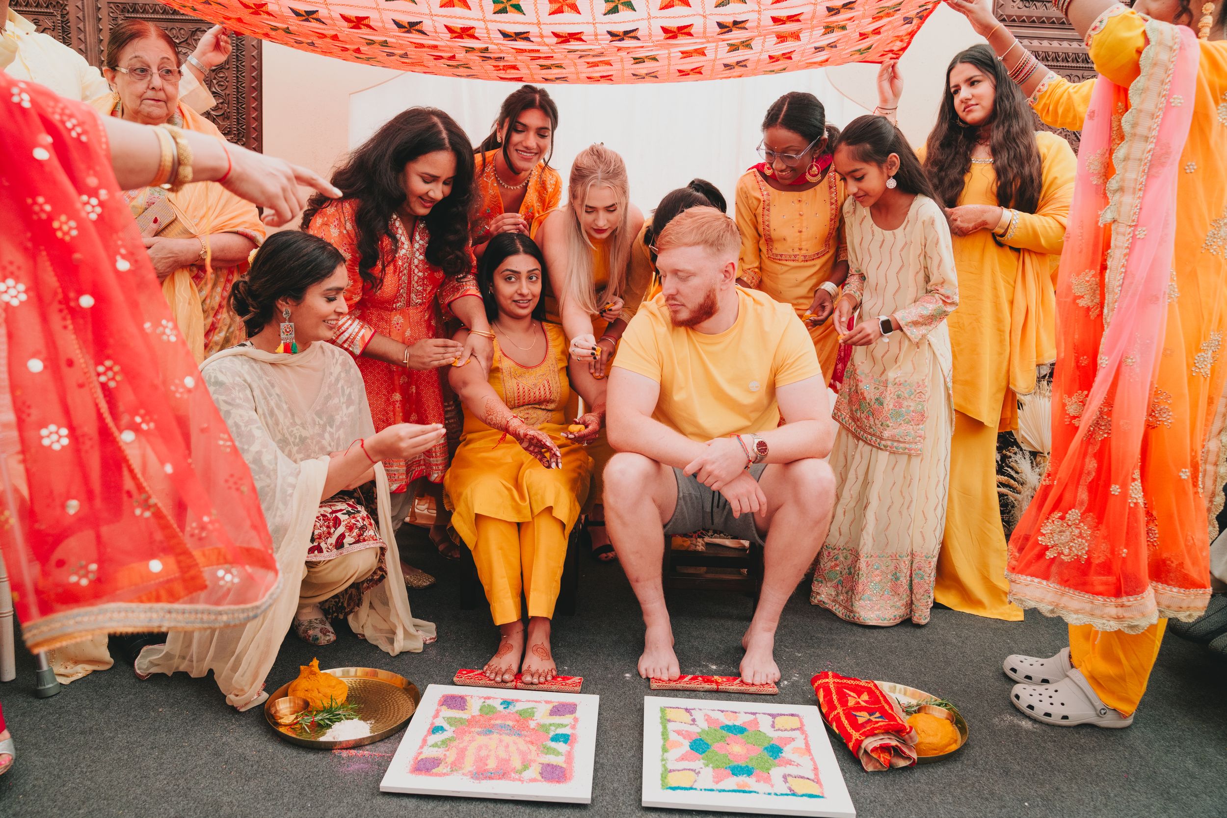Wedding guests in yellow and cream outfits gather for traditional Indian wedding games and ceremonies.