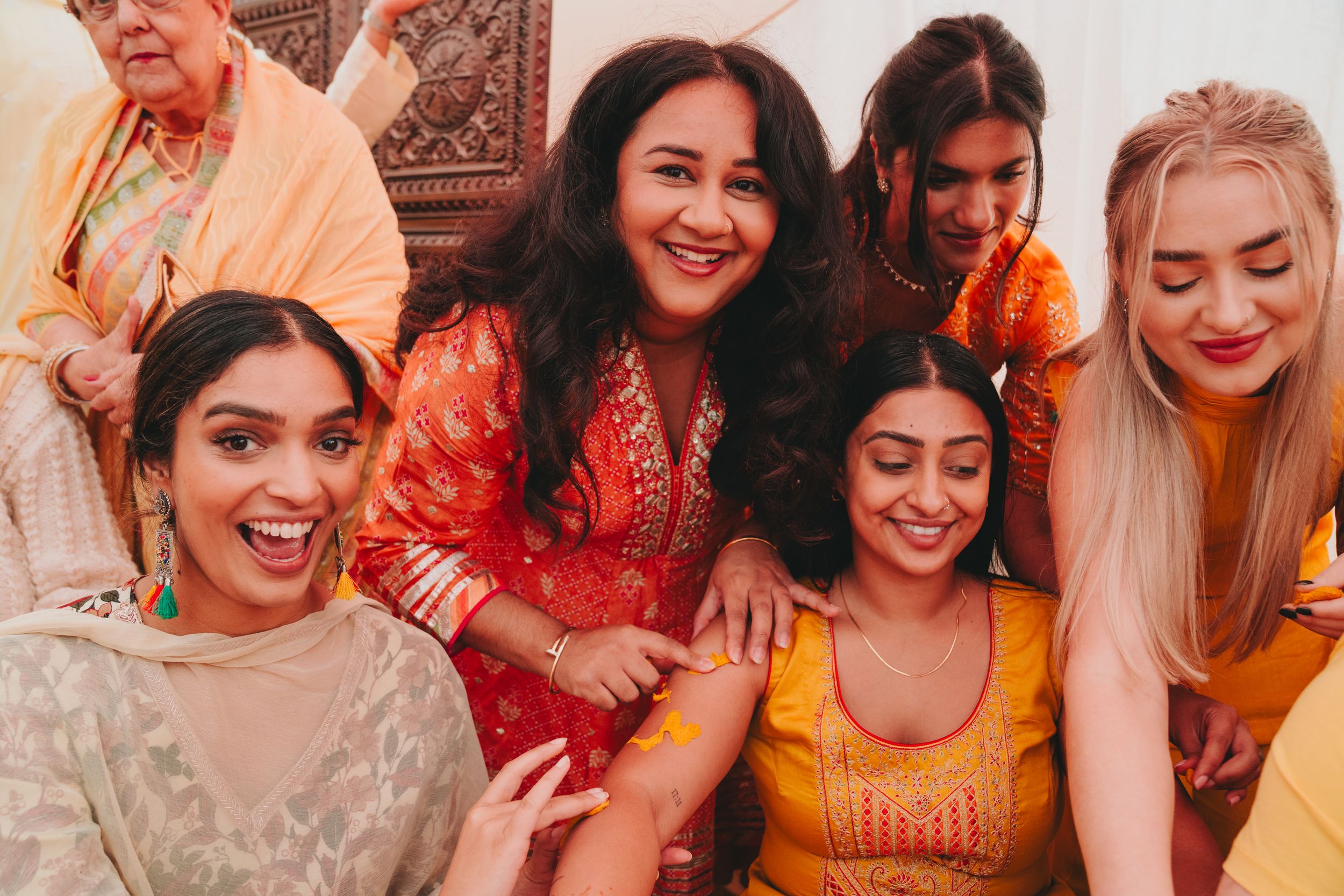 A joyful gathering of friends wearing traditional Indian attire in warm yellow and red tones at a celebration.
