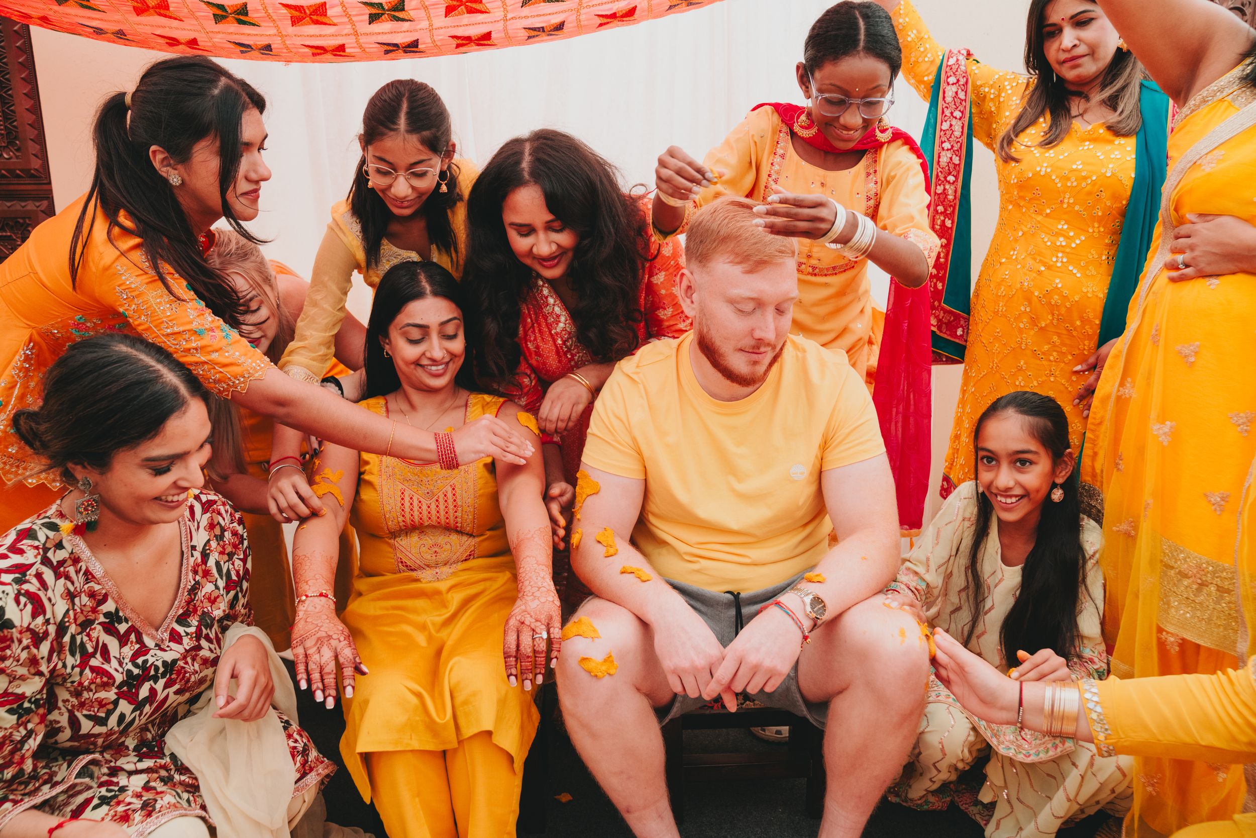 A group celebrates wearing vibrant yellow and orange traditional Indian outfits while sharing laughter together.