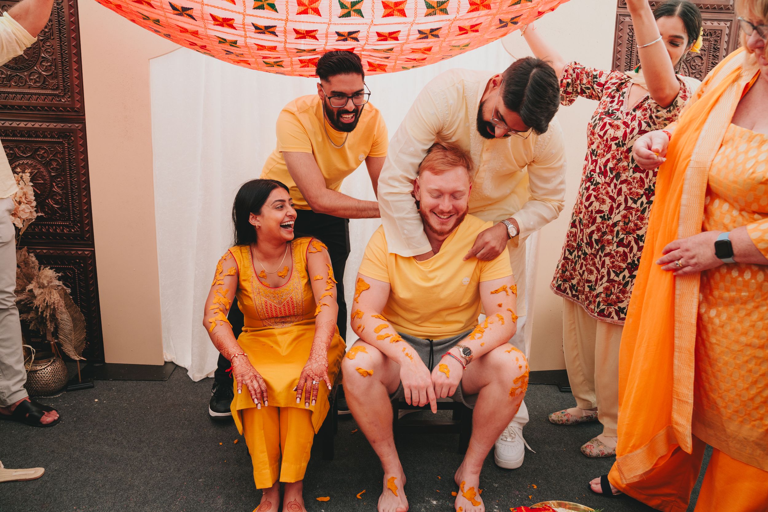 A festive celebration scene with people wearing traditional yellow and orange Indian attire.