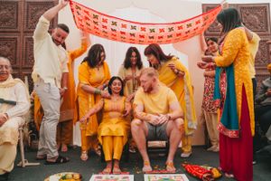 Celebratory gathering with people in yellow and orange traditional dress under decorative red banners.
