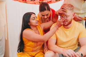 Friends participate in a traditional ceremony with turmeric paste application during an Indian celebration.
