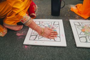 Close-up of hands applying color to a decorative tile pattern during a traditional ceremony.