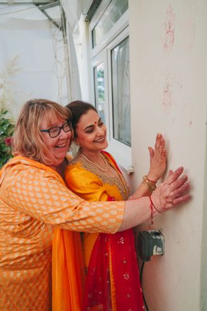 Two people in traditional orange and red attire press their hands against a white wall in celebration.