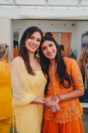 Two attendees in yellow and orange traditional outfits pose together at a cultural celebration.