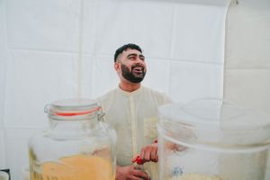 A person in light clothing smiles while standing between large glass jars during a celebration.