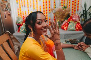 Person in yellow traditional dress shows off intricate henna designs on their hand during a celebration.