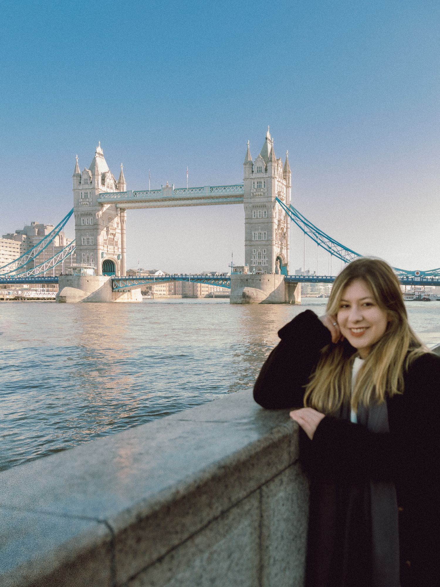 Tourist posing against Tower Bridge during golden hour in London.