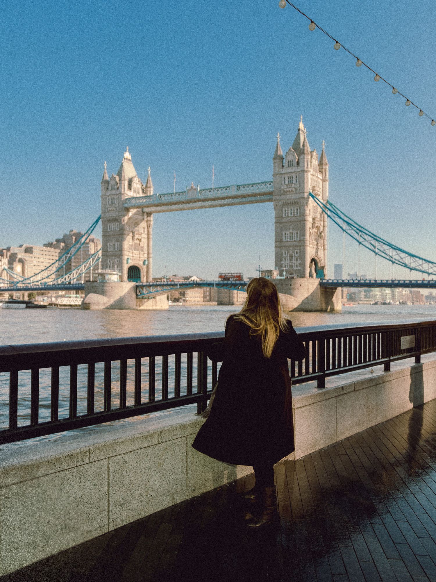 Tourist admiring the iconic Tower Bridge in London on a sunny day from a riverfront viewing area.