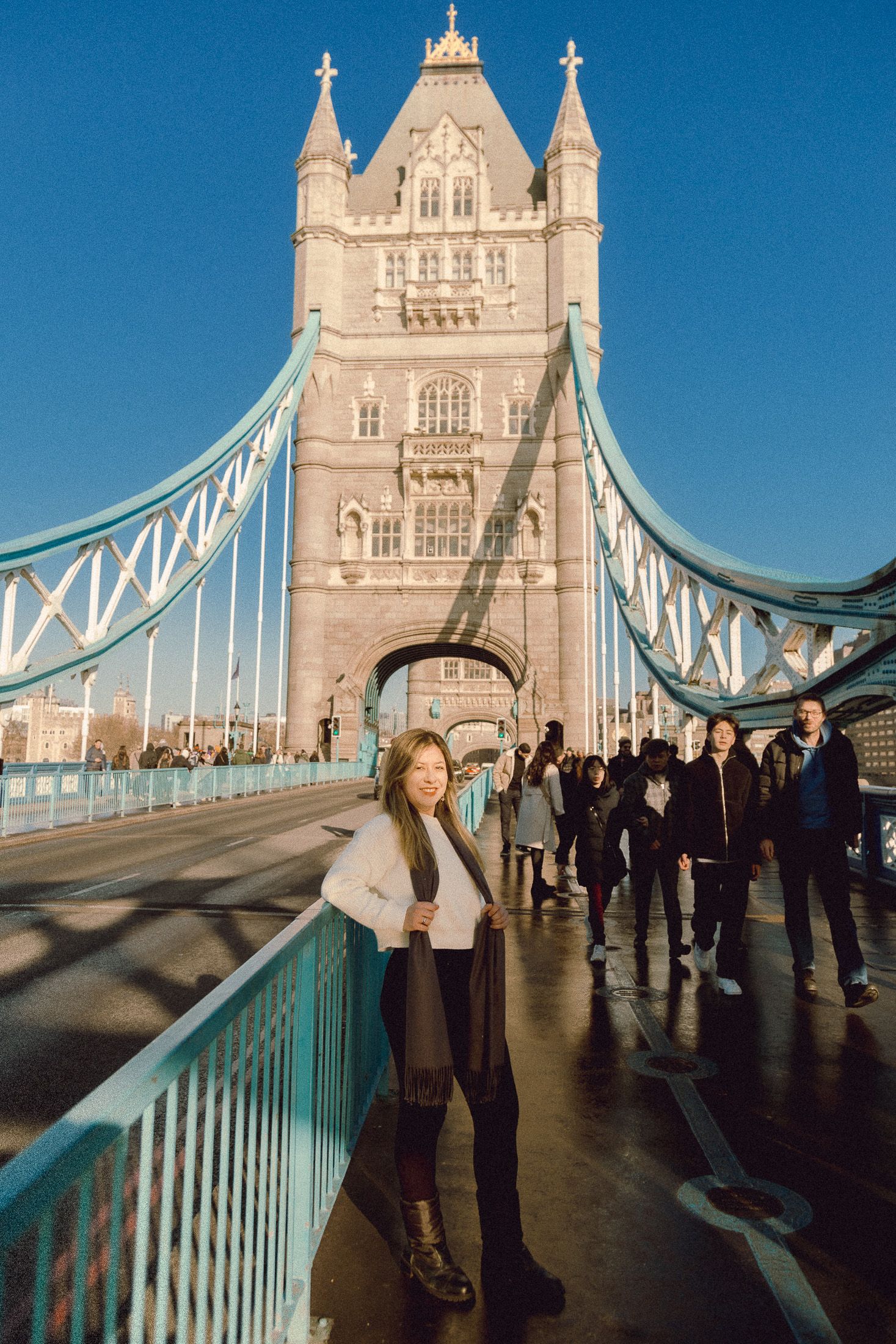 Winter fashion pose on Tower Bridge pedestrian path with iconic tower in background.