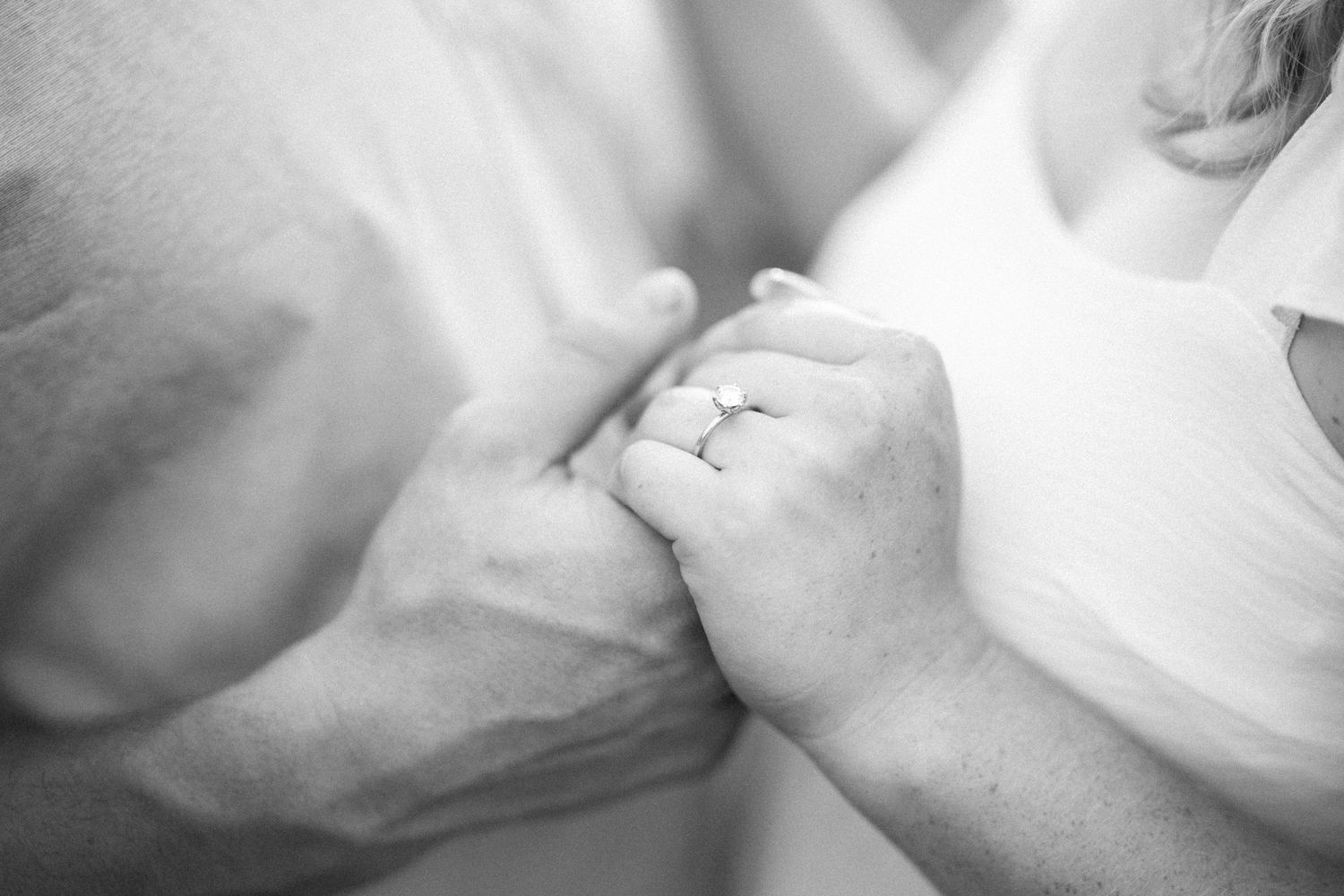 Close up black and white photo of hands kissing an engagement ring in an intimate romantic moment.