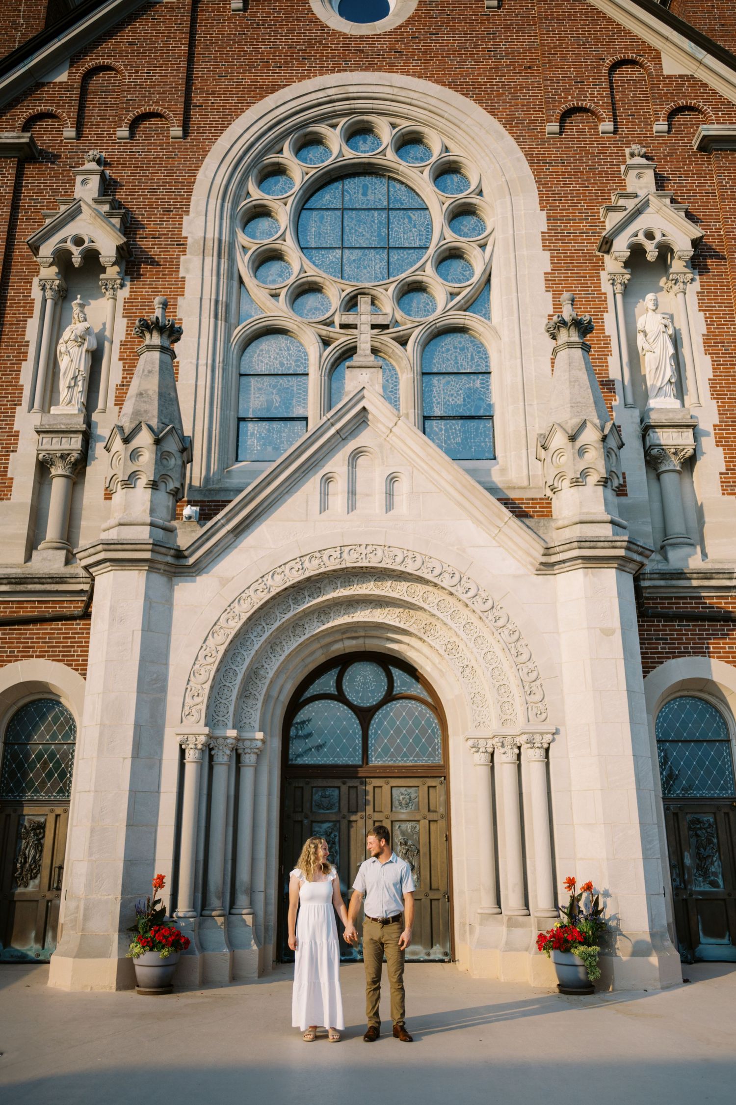 Two people stand in front of ornate Gothic church entrance with circular rose window and stone statues.