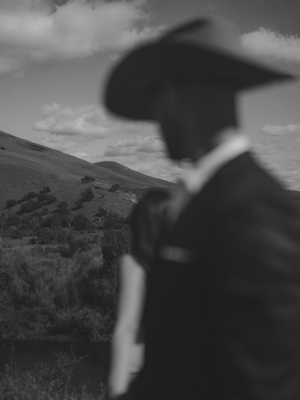 Silhouette figure in western attire gazes across rolling hills under dramatic clouds.