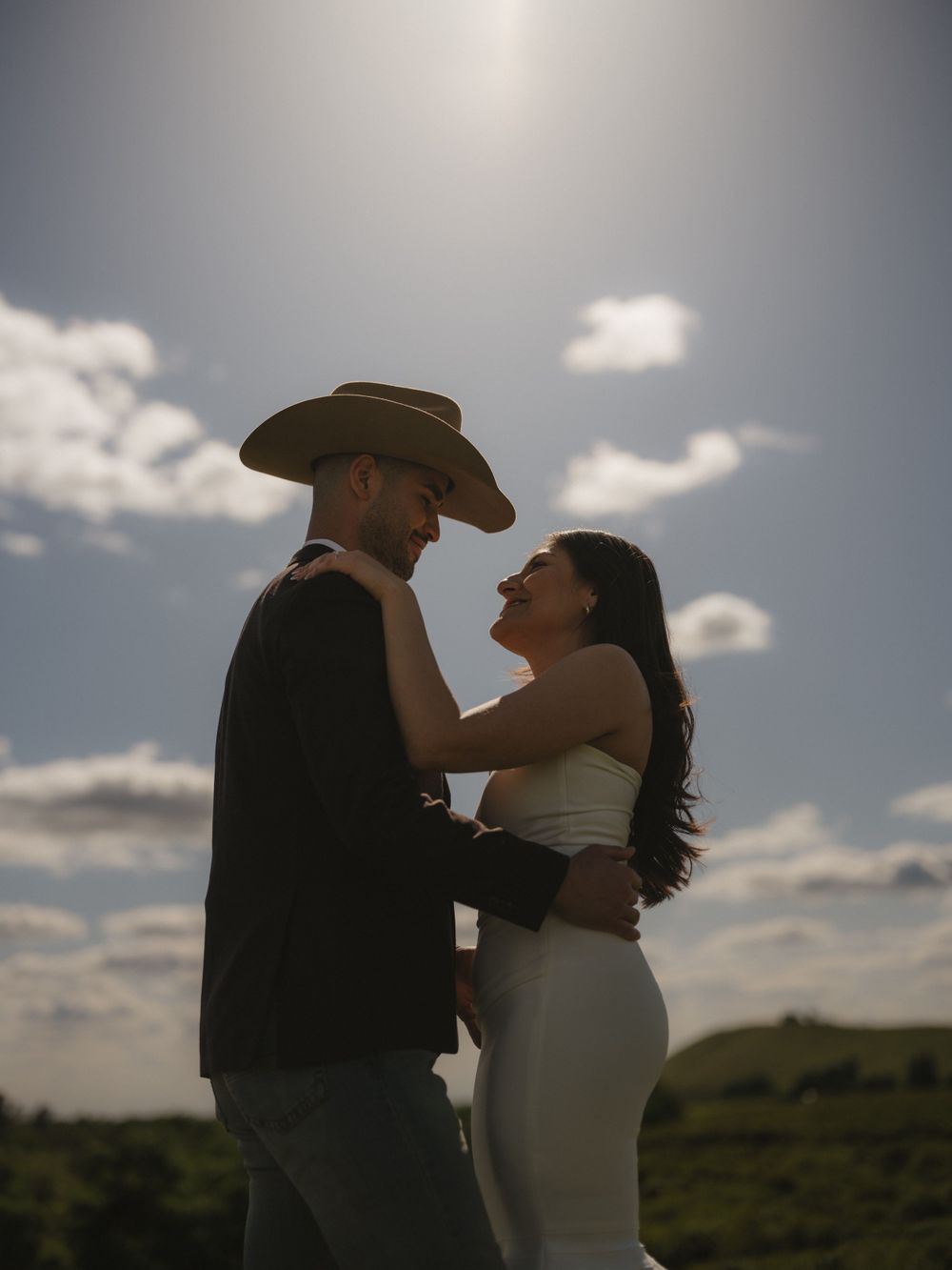 Couple in western formal wear share intimate moment under dramatic cloudy sky.