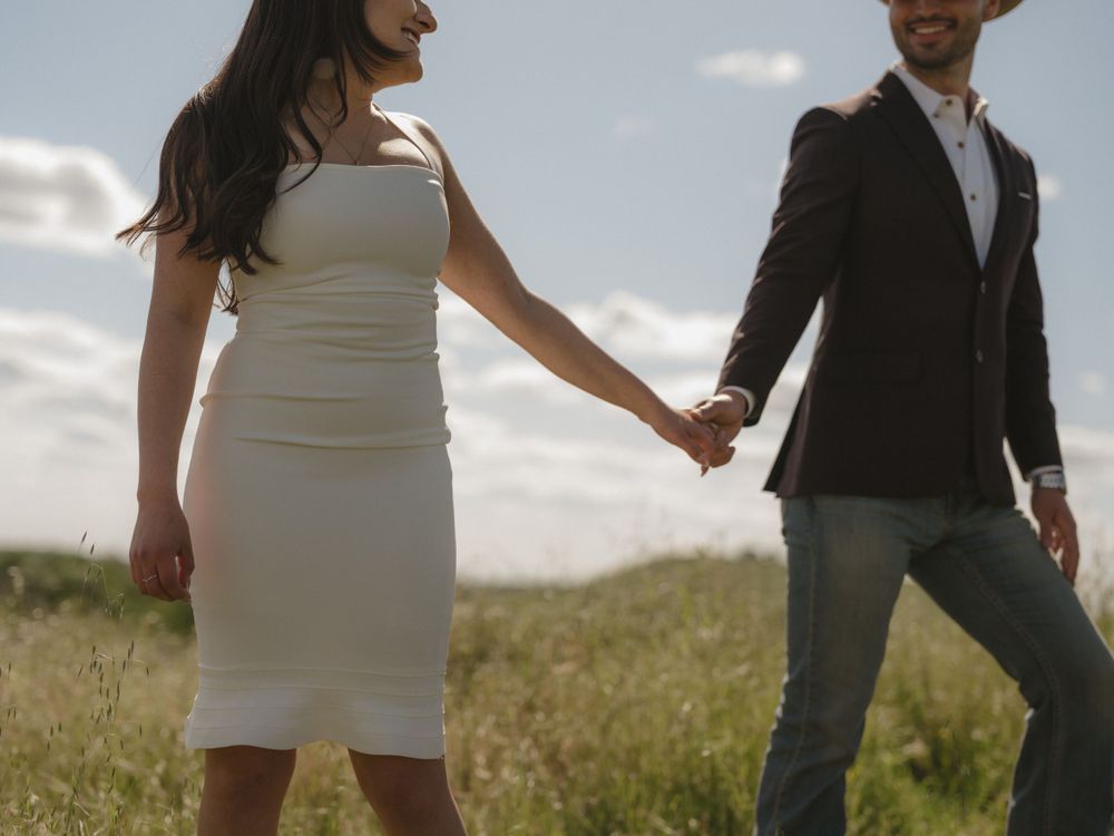 Couple in western attire holding hands while walking through meadow.