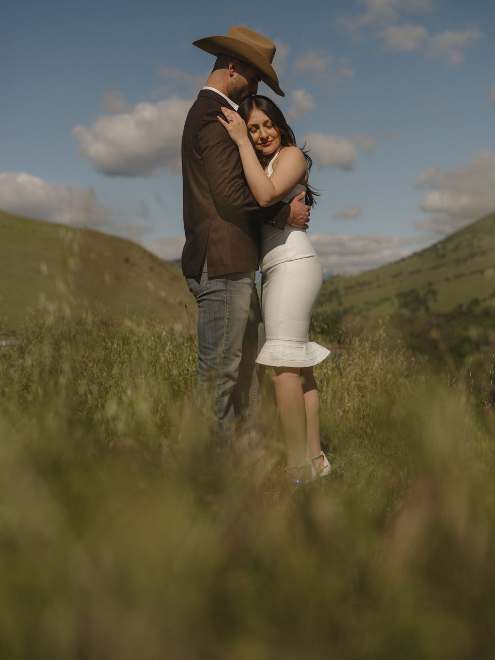 Intimate portrait of couple in western attire standing in tall grass.