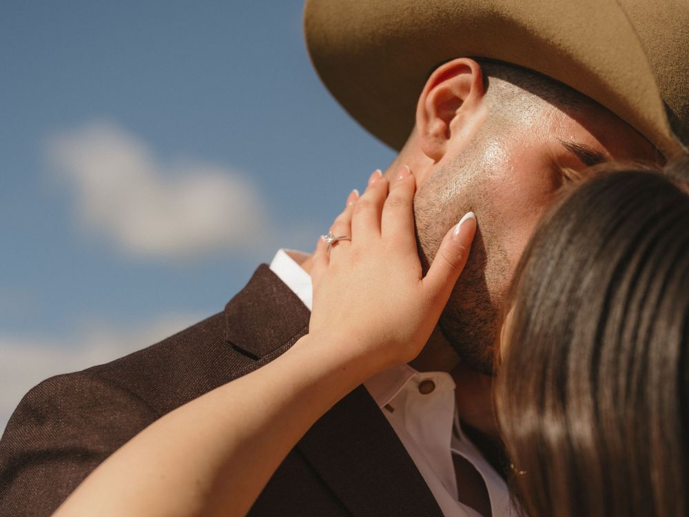 Intimate moment captured between couple in western-inspired formal wear against blue sky.