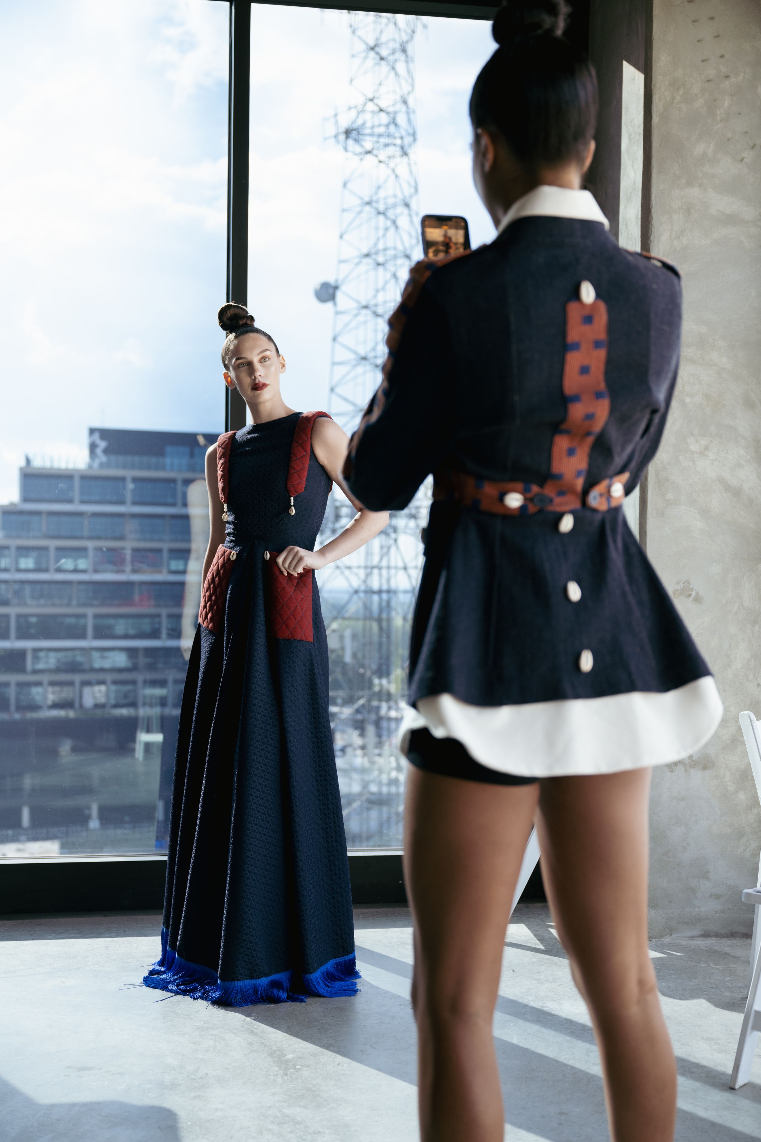 Fashion photo shoot with contrasting outfits in front of a window with city views.