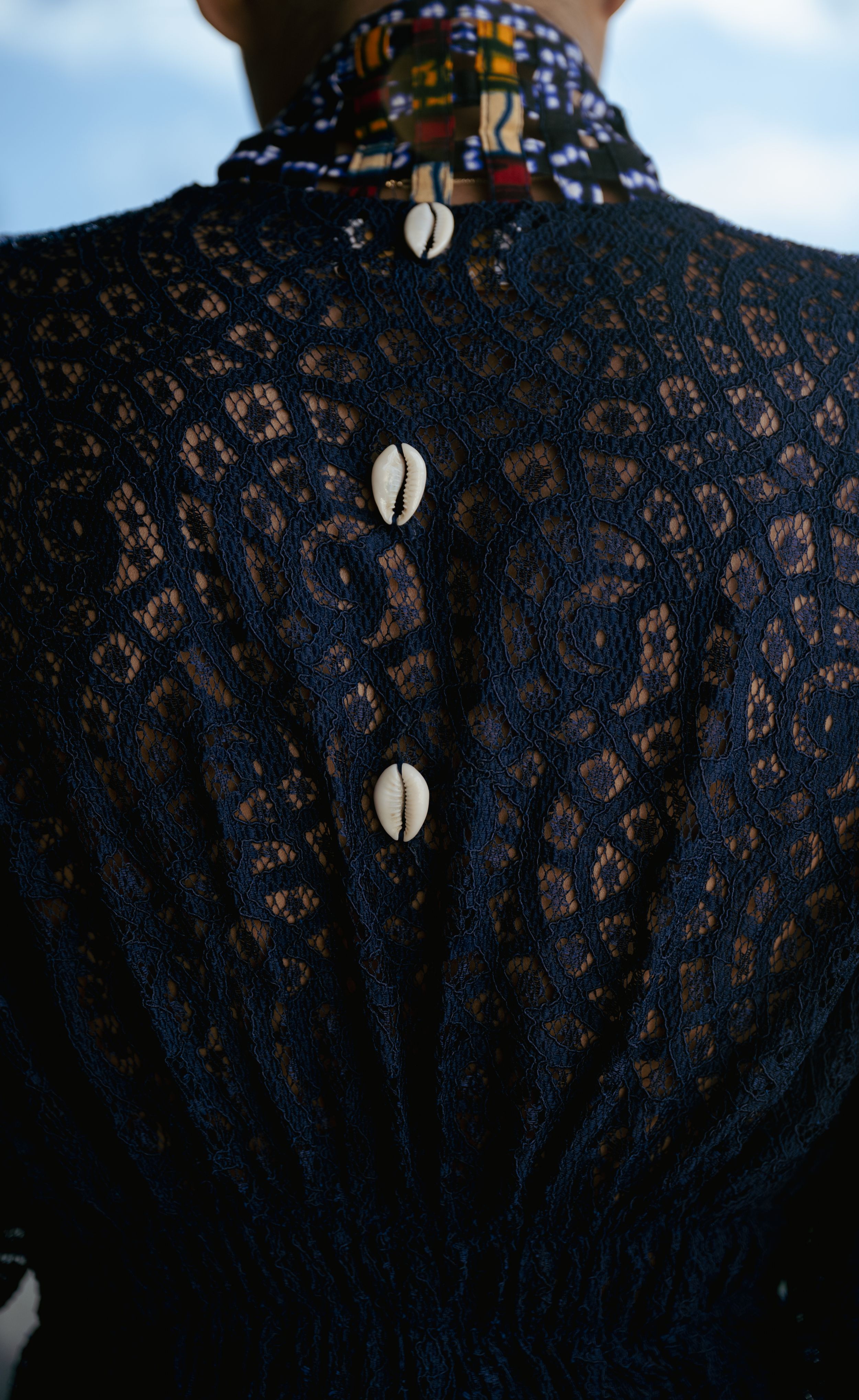 Close-up of black lace dress back detail with decorative shell buttons.