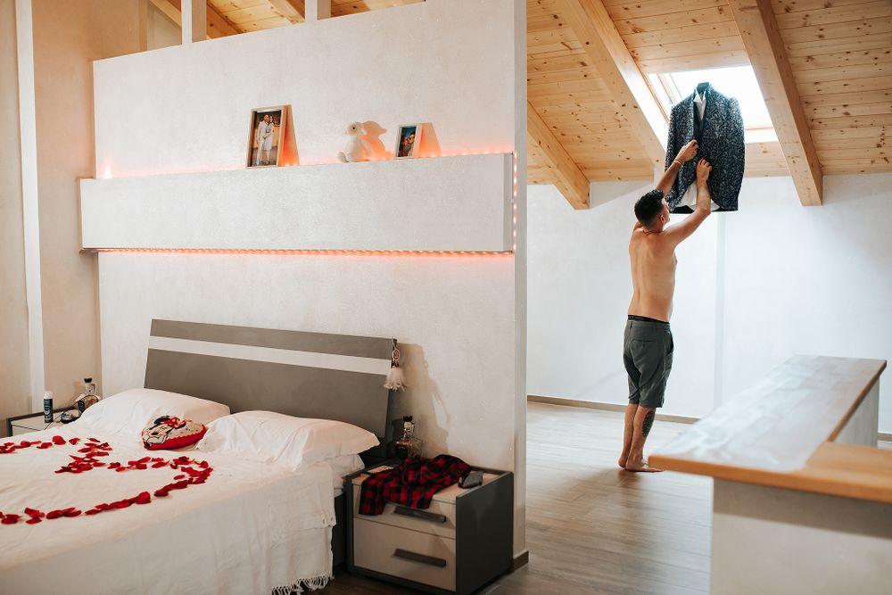 Groom getting ready in modern attic bedroom decorated with red rose petals on wedding day.